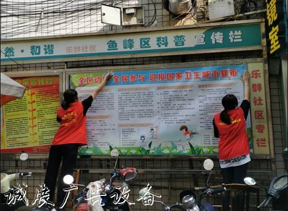圖為轄區(qū)志愿者正在粘貼創(chuàng)城板報
